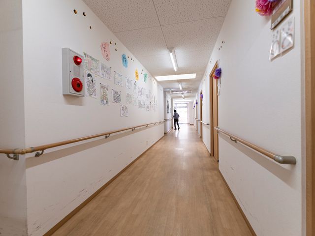 廊下に描かれた絵とスタッフ 廊下 明るく清潔な通路には個性的な絵画が飾られ、遠くに見えるスタッフの方が忙しく動いています。利用者の方々の心地よい日常の一コマを垣間見ることができます。