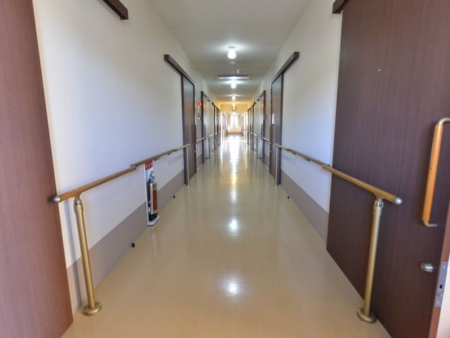 廊下の明るい風景 施設内の廊下 手すりが整備された安全な通路です。明るく清潔な空間で安心してお過ごしいただける環境が整っています。