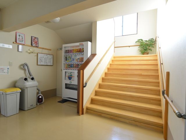 廊下の階段と自動販売機 階段 廊下の階段は手すりが設置され、安全に昇降ができる環境です。壁には掲示物があり、自動販売機が設置されています。