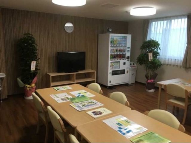 休憩室の様子 共有スペース 広々とした休憩室です。テーブルには資料が整えられ、壁際の飲料自動販売機も設置されており、利用者の方々はここで憩いの時間を過ごされています。