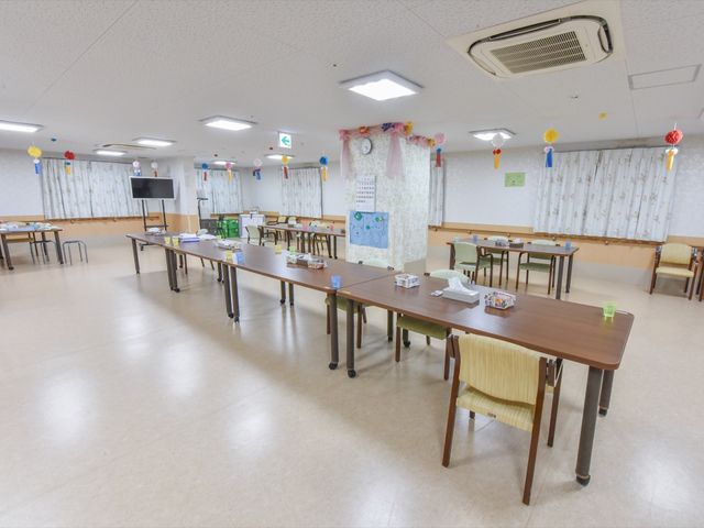 多目的スペースの広々とした雰囲気 共有スペース 広く開放的な空間で、利用者の方々のコミュニケーションの場となっています。明るい装飾が施され、温かみのある環境が特徴です。