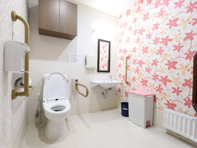 装飾的な壁のトイレ トイレ 手すり付きで花柄の壁紙が特徴的なトイレです。安全と使いやすさを考慮した設計で、快適な日常生活をサポートします。