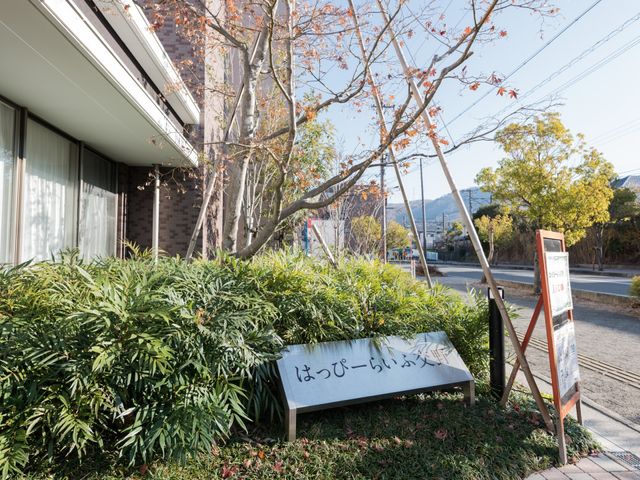 中庭の緑と看板 看板 温かみのあるエントランスが迎える施設には、周囲の自然と調和した心地よい空間が広がっています。