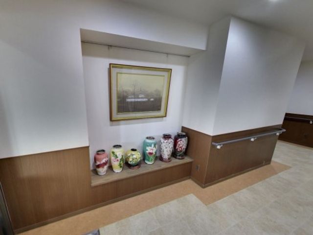 廊下に飾り棚と絵画 骨董品 手すり付きで安全な廊下に、彩り豊かな陶器と絵が飾られています。アートがある環境で働く魅力を感じてください。