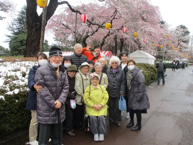 桜の下で笑顔の集合 バスツアー 広々とした中庭で、満開の桜のもと笑顔でポーズをとる皆さん。共に四季の美しさを感じられる素晴らしい環境です。