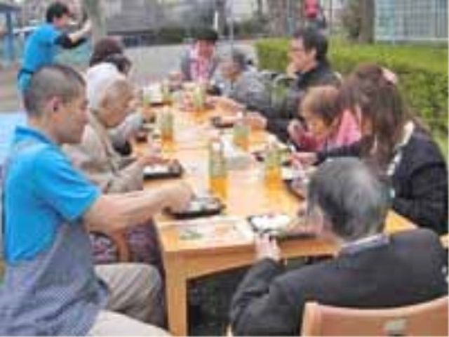中庭で食事する人々 レクリエーション 開放的な中庭で共に食事を楽しむ様子。スタッフも笑顔で対応しており、温かなコミュニティが感じられます。