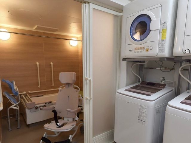 洗濯機と車椅子の設備 浴室 床や壁が明るく、清潔感のある浴室です。移乗用の車椅子も完備しており、安心してご利用いただけます。