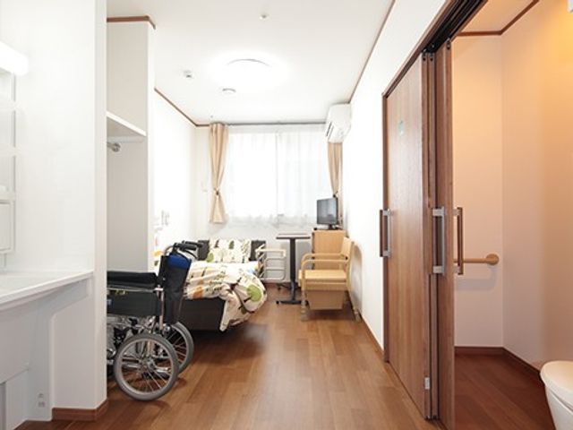 車椅子のある居室 居室   車椅子を置ける広さがあり、窓から光が入る明るい居室です。木目調の床で、落ち着いて過ごしやすそうです。