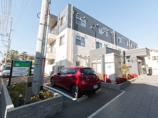 清潔感のある施設外観 駐車場 緑に囲まれた施設の入り口には、案内看板が設置されており、来訪者を温かく迎えています。