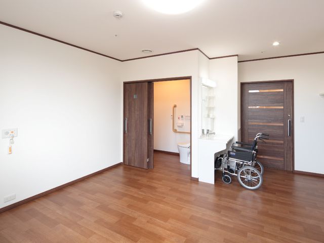車いすと洗面台がある居室 居室 広々としたフローリングの部屋で、車椅子ユーザーも動きやすい構造になっています。洗面台がすぐ近くにあり、日常の準備が便利です。