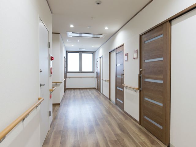 明るい清潔な廊下 廊下 手すりが備え付けられた安全な通路です。壁面には居室の名札が並んでおり、清潔感のある環境が整っています。