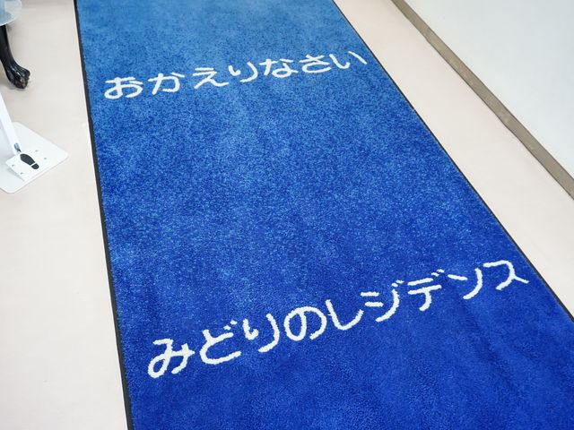 青いカーペットのエントランス マット ゆったりとした歓迎の気持ちが伝わるエントランスです。温かみのある空間で皆様をお迎えします。