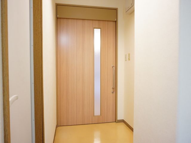 廊下に面した木製のドア 居室 明るく清潔感のある廊下に設けられた居室の入口です。プライバシーを確保しつつ、明かり取りの窓が設置されています。