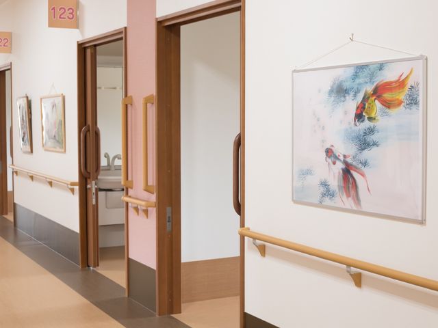 廊下の壁画と扉 通路 番号が示された明るい廊下は、アートで飾られ落ち着いた雰囲気です。手すりも完備され、安全な歩行をサポートしています。