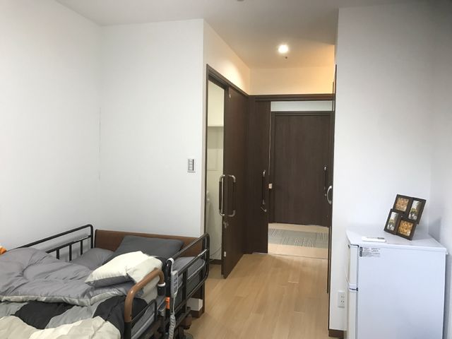 清潔な居室の模様 居室 広々とした居室には、手に馴染む木の扉があり、明るい雰囲気の中で生活ができそうです。必要なものがすぐ手に取れるよう、ベッドサイドには小さな冷蔵庫も設置されています。