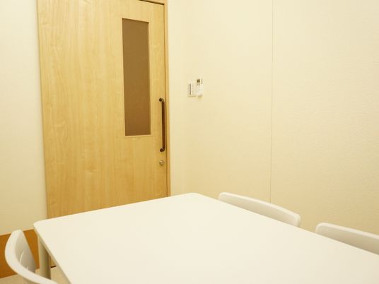 淡いベージュの木目調のスライド式ドアのついた部屋。壁はアイボリーで、置かれたテーブルは真っ白。同じく真っ白な椅子も設置されている。