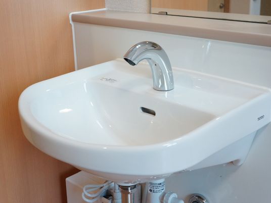 洗面台のアップ画像。白く清潔に保たれている様子が分かる。自動で給水止水ができるタイプで、鏡や小物を置く台も付いている。