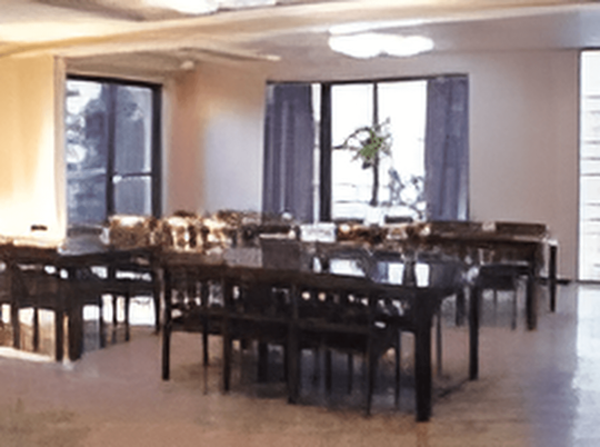 施設の写真 濃い色のテーブルと椅子が並べられている、２面に窓がある食堂