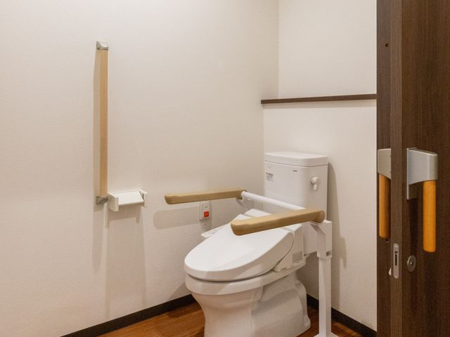 手すり付きトイレ トイレ   手すりが複数あり、立ち座りを支えやすいトイレです。木目調の床で、落ち着いた印象です。
