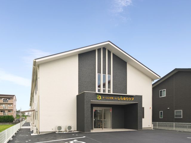 新築そうな施設の外観 スタッフと思われる方が入口で笑顔で接しており、明るい雰囲気の施設です。現代的なデザインの建物は、就業環境としても魅力的でしょう。
