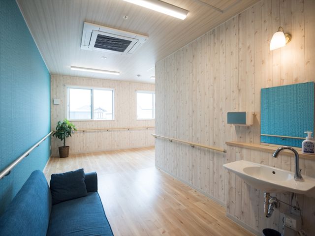 清潔な居室の角部分 共有スペース 広々として清潔感のある部屋です。手すりが設置されており、ゆったりとしたソファも完備されています。