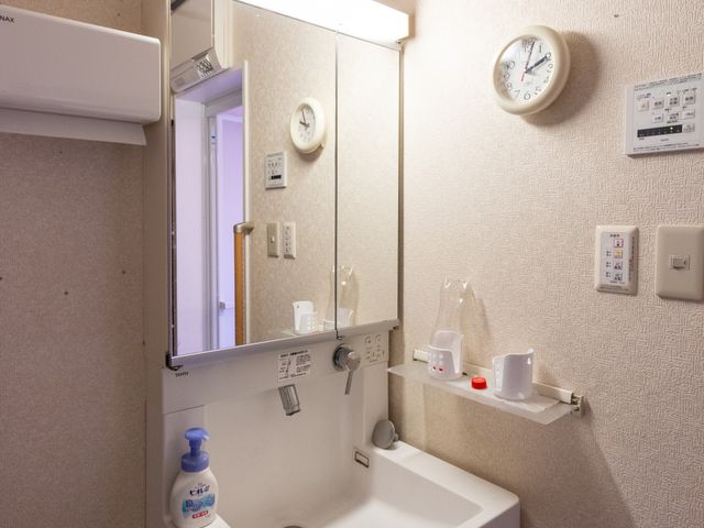 清潔な洗面台の風景 洗面台 壁には時計があり、必要な日用品も整った洗面スペースです。利用者の快適な生活をサポートします。