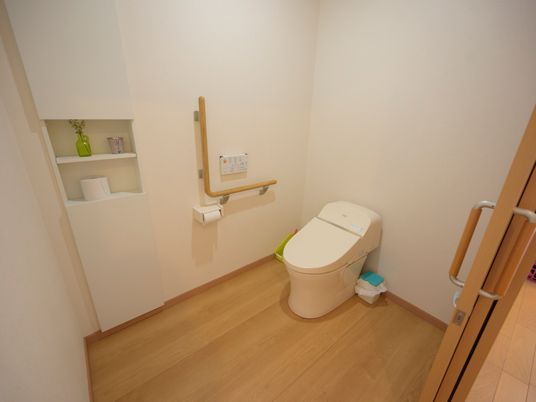 施設の写真 フローリングに白い壁で、清潔感のあるトイレ。引き戸になっていて中が広く、壁には手すりがある。