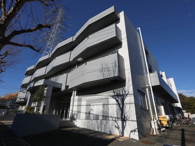 白い外壁の建物外観 外観 清潔感のある外壁が印象的な施設で、窓も大きく日当たりが良さそうです。緑が植えられたアプローチも心地良い空間を演出しています。