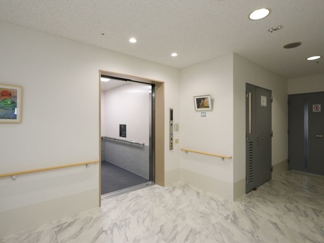 清潔な廊下とエレベーター エレベーター 手すりが備わった廊下を進むと、自動開閉式のエレベーターが設置されており、移動の利便性が考慮された設計です。