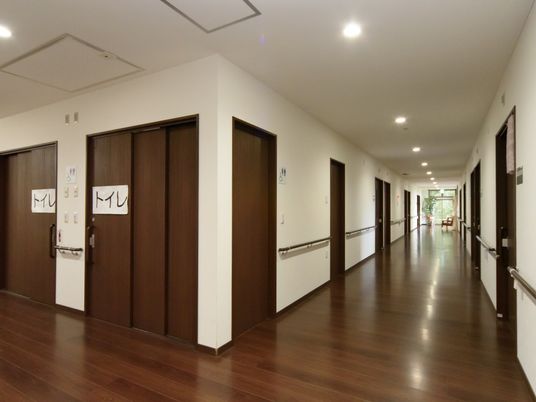 幅広の廊下である。居室やトイレが両側に設けられている。右奥の掃き出し窓の側には、椅子と観葉植物が置かれている。