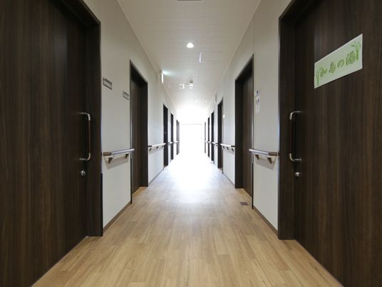 フローリング敷の廊下は、建具の色が統一されており、深みのある空間となっている。壁には木製の手すりが設置されている。