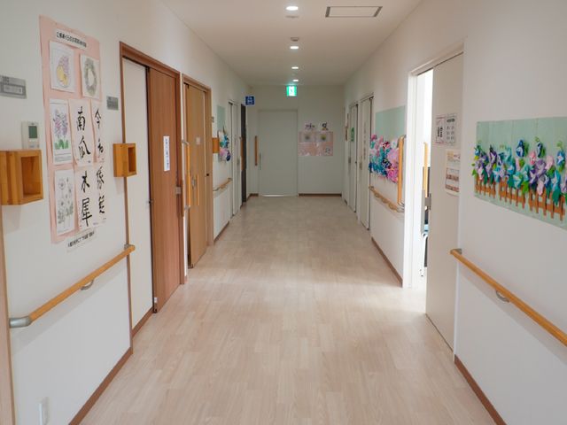 明るく清潔な廊下 廊下 手すりが設置された安全で明るい廊下です。壁の掲示物や装飾が温かみのある雰囲気を演出しています。