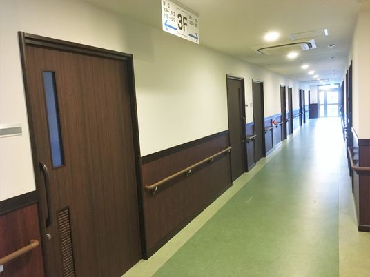 濃い色合いのドアがついた施設の居室入り口。廊下にはまんべんなく手すりが取り付けてある様子