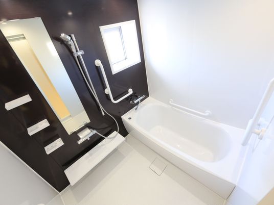 白い壁と、洗い場部分が黒い壁になっている浴室がある。小窓が付いており、壁には手すりが設置されている。