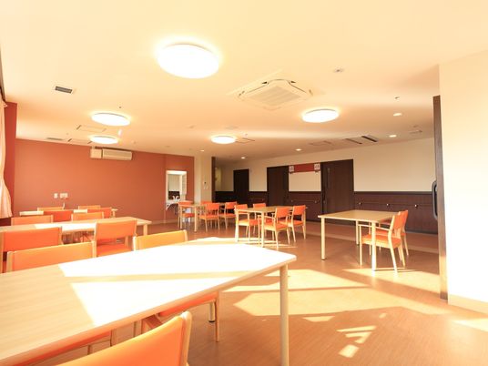 壁の一部がライトブラウンになっている、広く明るい食堂がある。ブラウン系のテーブルと椅子が並んでおり、天井にはシーリングライトが付いている。