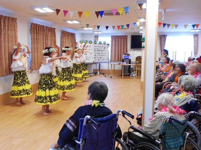 フラダンスを観賞するホール 多目的室 華やかなフラダンスのイベントが行われています。入居者の方々がリラックスして楽しめる空間です。