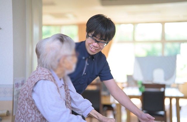 和やかな交流風景 リビング 広々とした空間で、スタッフと利用者の方が和やかに会話を楽しんでいます。自然光が差し込み、明るい雰囲気です。