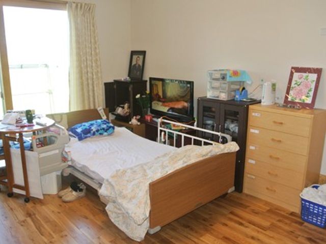 明るい居室のベッド 居室   大きな窓から自然光が入る、明るい居室です。ベッドやテレビ、収納家具があり、落ち着いて過ごしやすそうです。