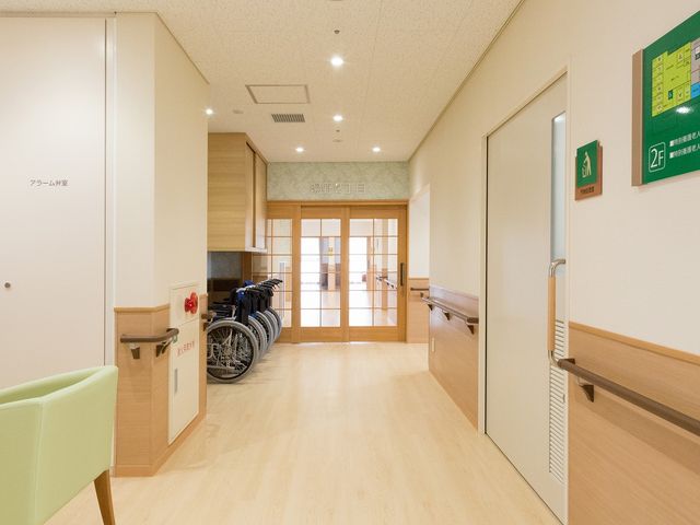 明るい廊下 廊下 ゆったりとした明るい廊下です。壁には掲示物があり、車椅子も置かれています。