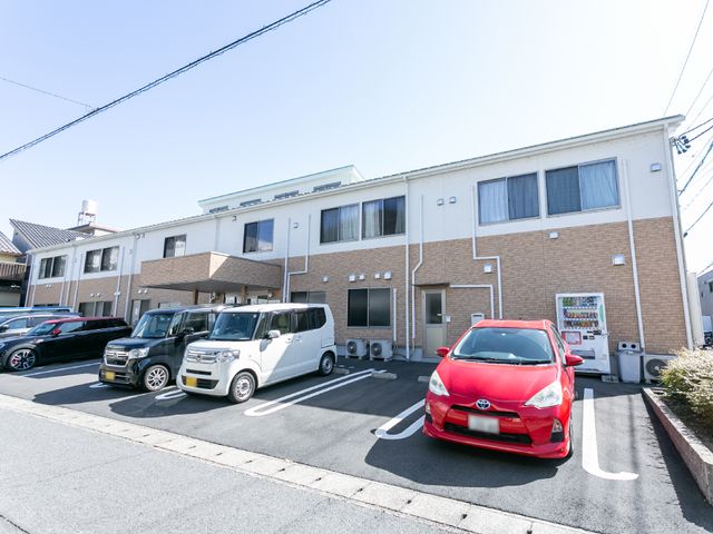 施設の清潔な外観 外観 広々とした駐車スペースが確保された建物前です。気持ちの良い青空の下、訪れる方々を迎える準備が整っています。