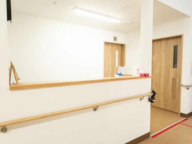 壁に手すり設置された廊下 廊下 手すりが備えられた廊下は、安全に配慮された設計です。清潔感のある床と木目調のドアが、落ち着いた雰囲気を醸し出しています。