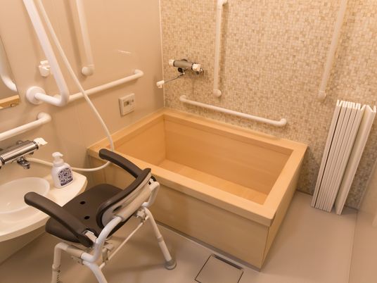木製の浴槽が設置された浴室がある。壁には手すりが備え付けられていて、洗い場にはシャワー椅子が置かれている。