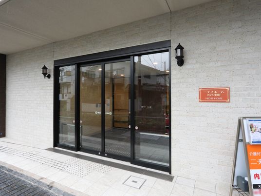 施設の玄関の前のスペースに屋根が設置されており、通路には点字ブロックがある。扉は自動ドアでガラス張りになっている。