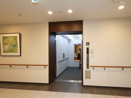 エレベーターの扉が開いており、奥に縦長の鏡が見える。通路の壁には手すりが取り付けられ、操作パネルの液晶部に１階であることが表示されている。