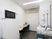 サムネイル 白い壁に囲まれた健康管理室である。長テーブルに椅子が２脚置かれ、冷蔵庫や電子レンジが設置されている。聴診器が壁にかかり、ワゴンもある。