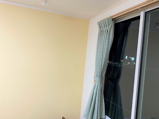 居室の一角とベッド 見守りシステム ゆったりとしたベッドが配置され、落ち着いた色合いの部屋です。日々の生活に安心感を提供する空間です。