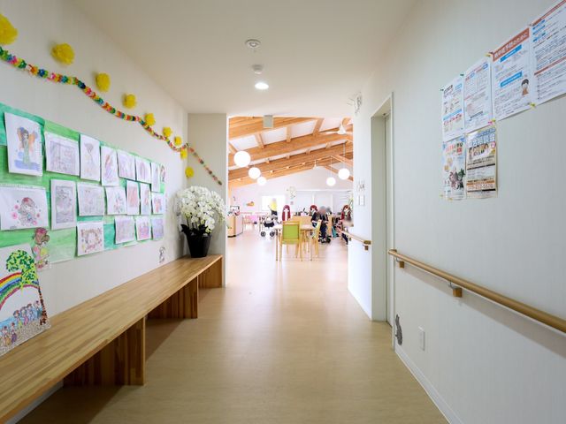 廊下に飾られた作品と掲示物 廊下 活気ある廊下には季節感のある作品が飾られ、遠くではスタッフと利用者の優しい会話が見られます。安全配慮の手すりも完備されています。