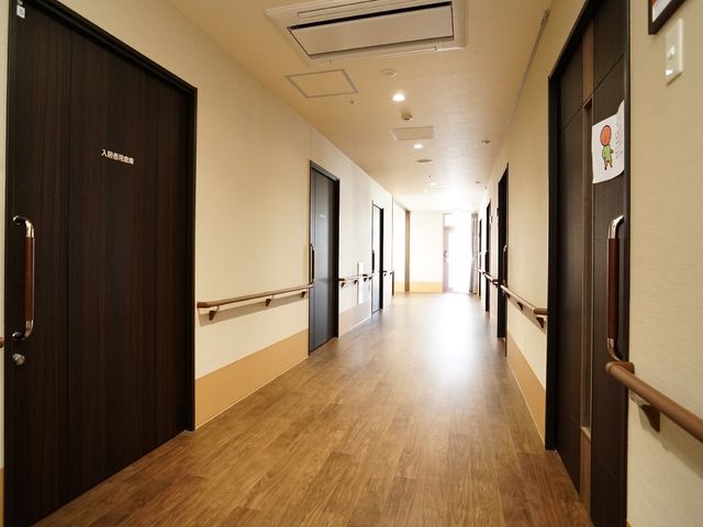 廊下の明るい様子 廊下 手すりが設置された落ち着いた色合いの廊下です。安全かつ快適な移動をサポートし、働く環境としても整っています。