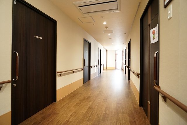 廊下の明るい様子 廊下 手すりが設置された落ち着いた色合いの廊下です。安全かつ快適な移動をサポートし、働く環境としても整っています。