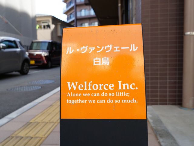 橙色看板のクローズアップ ロゴ 「WelforceInc.」と書かれた橙色の看板が目印です。一人では小さなことしかできませんが、皆で協力すれば大きなことができます。